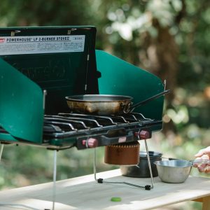 A portable gas stove with pan and equipment outdoors, perfect for camping cooking.