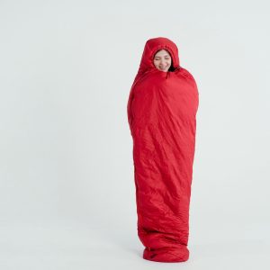 A young woman wrapped in a red sleeping bag, smiling with a serene expression.