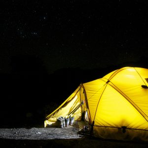 A glowing yellow tent pitched outdoors under a vast, star-filled night sky, capturing the essence of camping adventure.
